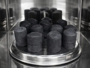 Black cylindrical rubber compounds arranged on a stainless-steel rotating tray inside an industrial microwave processing chamber.